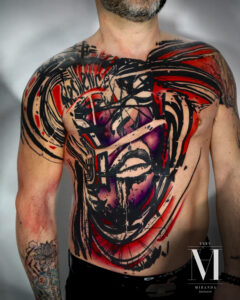 tatuaje en el pecho y tatuaje en el brazo en negro y rojo hecho por abel miranda, representa una cara humana dividida en tres bloques y un fondo dinamico y caotico.